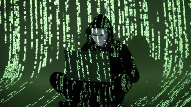 Haker siedzący po turecku w ciemnym pokoju, otoczony zielonym kodem i patrzący w ekran laptopa