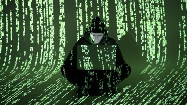 Zamaskowany haker w czarnej bluzie pracuje przy laptopie z kodem matrix &ndash; cyberprzestępczość, bezpieczeństwo IT, ciemna sieć, cyberatak, kod binarny, hakowanie, darknet, cyberświat, haking