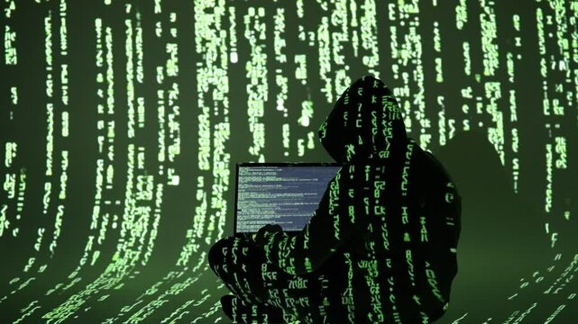 Zamaskowany haker w ciemnym kapturze pracuje przy laptopie otoczony kodem matrix &ndash; cyberprzestępczość, cyfrowe włamanie, cyberatak, dark web, bezpieczeństwo IT, cyberświat, złośliwe oprogramowanie