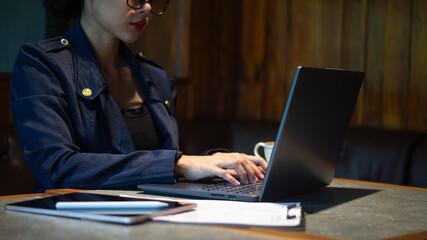 Confident businesswoman typing something on laptop on conference room table, tablet and paper on it, gloomy atmosphere, stressed manager working