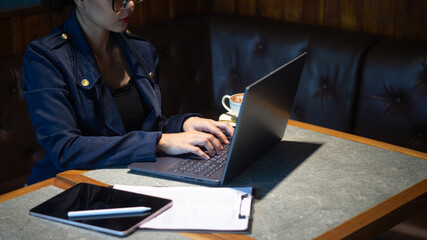 Confident businesswoman working on laptop on coffee shop table with tablet and paper, cafe manager managing store information