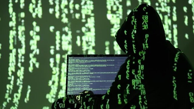 Zamaskowany cyberprzestępca w czarnym kapturze pracuje przy laptopie wśr&oacute;d zielonego kodu matrix &ndash; cyberatak, hakowanie systemu, dark web, haker w akcji, bezpieczeństwo cyfrowe, kodowanie danych