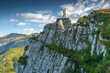 Male hiker carefully descends rocky cliff in the mountains with trekking poles, with scenic...