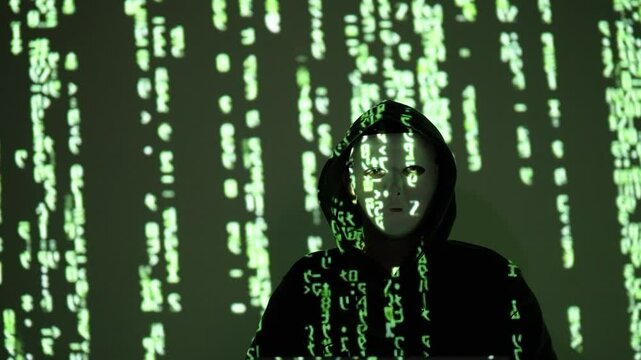 Zamaskowany haker w czarnym kapturze na tle kodu matrix w zielonym świetle &ndash; cyberprzestępczość, cyberbezpieczeństwo, tożsamość cyfrowa, atak hakerski, ciemna sieć, ciemny internet