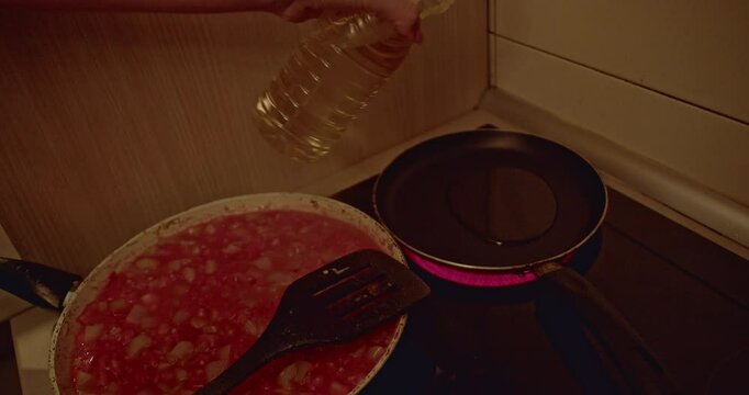 Cooking a meal in a pan on a stove. Oil is poured into a hot pan. The cook stirs a pan of diced tomatoes.