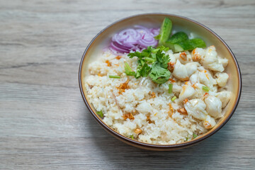 Garlic fried rice in a brown burnt ceramic plat topped with steamed crab meat, shallots and cucumber  on wooden table, Top view.
