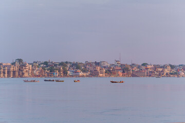 A peaceful morning view of Varanasi city across the Ganges River, with small boats floating gently on the calm water.