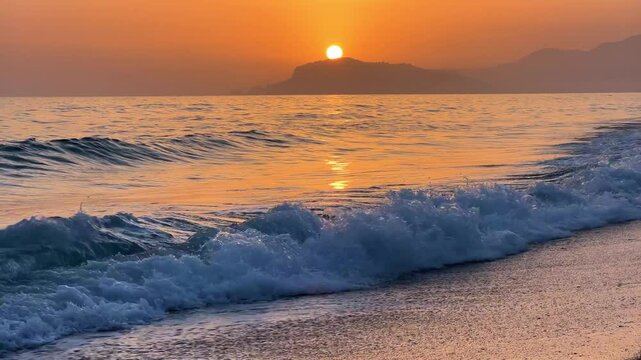 Sunset in Turkey, Alanya. The waves of the Mediterranean Sea roll over the sandy beach. The sunset is reflected in the water and slightly illuminates the city, against the background of Castle Hill.4К