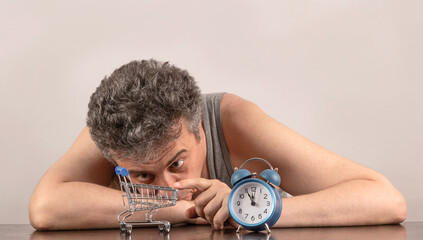 Conceptual story about poverty with a gray-haired middle-aged man and a miniature empty shopping...