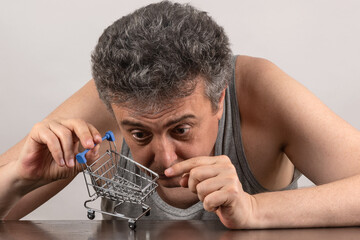 Conceptual story about poverty with a gray-haired middle-aged man and a miniature empty shopping...