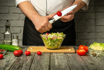 A chef skillfully chops vegetables while preparing a fresh salad. Ingredients on the wooden table include lettuce, cucumbers, tomatoes, and radishes, showcasing a vibrant kitchen atmosphere