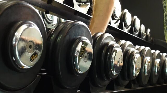 A man takes a dumbbell from the rack in a gym