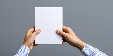 Hand holding a white sheet of paper on a gray background.