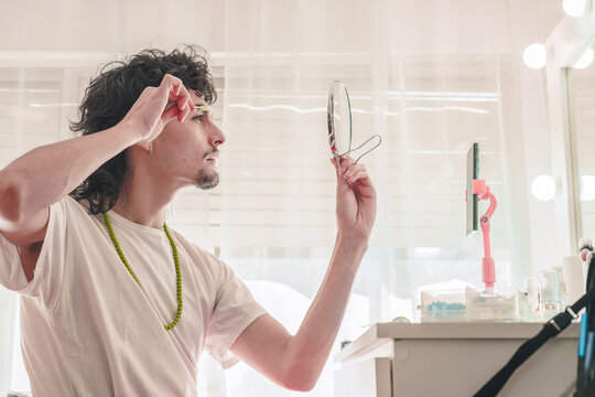 Young man plucking eyebrows looking at a small mirror and recording with smartphone