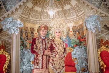 Obraz premium Elegant Minangkabau couple on their wedding day in traditional West Sumatran attire, adorned with gold elements and symbolic headpieces.