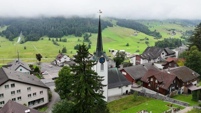 7 juli 2025, Wildhaus-Alt Sint Johann, Switzerland. Aerial view, drone flight in town during cloudy summer day. Near Alpstein mountains, flight towards church in the centre of the village.
