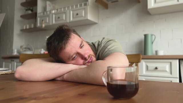 Sad tired sleepy young man with a cup of coffee at the kitchen feeling exhausted, yawning