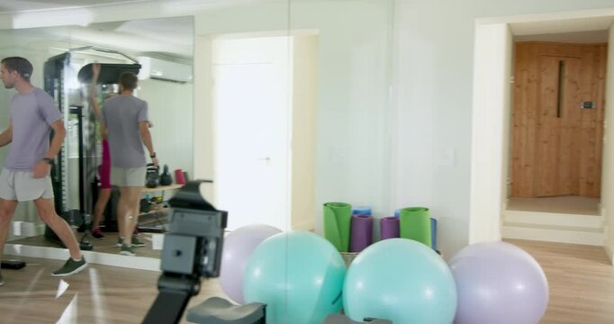 Couple exercising at home gym, woman using pull-up bar, man giving guidance