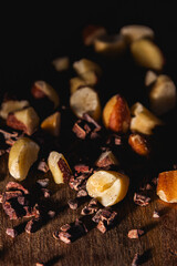 Close-up of chopped Brazil nuts and cacao nibs scattered over a rustic wooden surface in warm low light