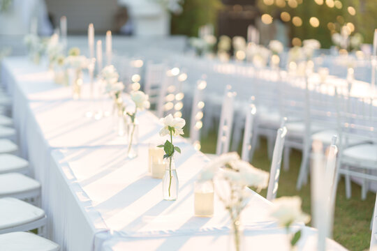 Elegant wedding long table with candle, white rose flower and white chairs in the garden