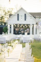 Elegant wedding long table with candle, white rose flower and white chairs in the garden