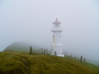 A famous mysterious lighthouse of the Mykines island during fog evokes remoteness and solitude of the place in the middle of Atlantic ocean at the end of the world on Faroe Islands, Denmark