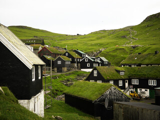 Typical faroese wooden houses with grassy roofs  hides under mountain. This village at the edge of Atlantic ocean called Mykines evokes remotennes, solitude and harsh life on the Faroe Island
