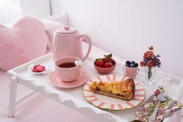 A beautiful delicious breakfast on a bed in white and pink tones. Natural light enters through the...