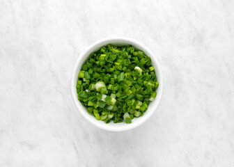 Bowl with chopped green onions, ceramic bowl with spring onions on white marble background, top view