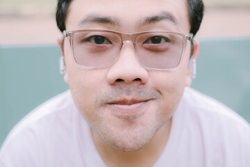 Smile Southeast Asian man wearing glasses, white T-Shirt and earbuds. Close up with bokeh background.