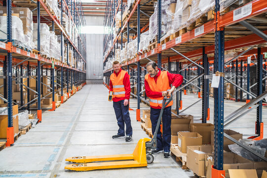 Warehouse workers moving goods on pallet jack in large distribution center, ensuring efficient product handling and timely delivery