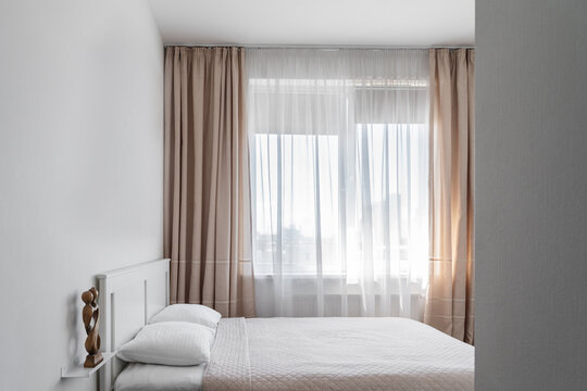 minimalistic design of a modern bedroom in white shades. a double bed with a wooden headboard, clean white linens and pillows.