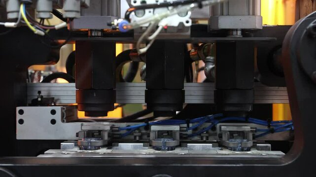Close up of plastic PET bottle preform heating process in industrial manufacturing machine. Automated industrial PET bottle machine. Robotic system automation in high speed plastic bottle production.