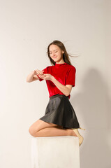 A sexy brunette in a short skirt on a light background counts money.