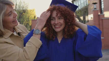 Proud mother gently adjusting graduation cap, sharing emotional moment of academic milestone and familial connection during daughter's educational achievement celebration