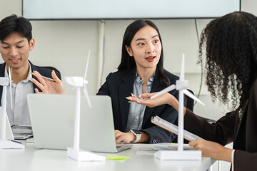 Discussion and Innovation in Sustainability. A diverse team collaborates on sustainable energy solutions using wind turbine models in an office setting.