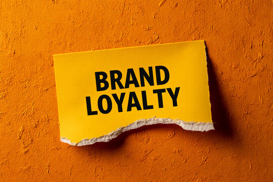 Torn yellow paper on orange background displays text: Brand Loyalty, showcasing a concept of customer commitment and brand recognition