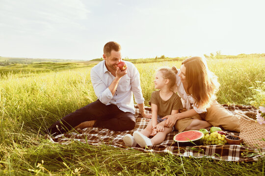 Holiday Concept. Young lovely family relaxing in the meadow, playing with fruits on a sunny day - Powered by Adobe