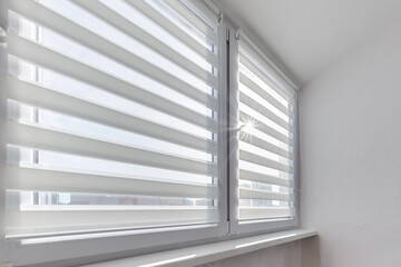 Modern double roller zebra blinds on large windows in bright minimalist interior with sunlight streaming through on balcony