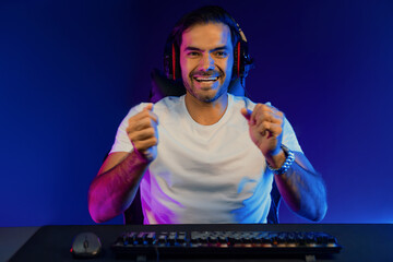 Winner of smart streamer playing online game wearing headphones raising fist up on streaming gamer with social media. Esport skill team player online digital gaming at neon light studio room. Surmise.