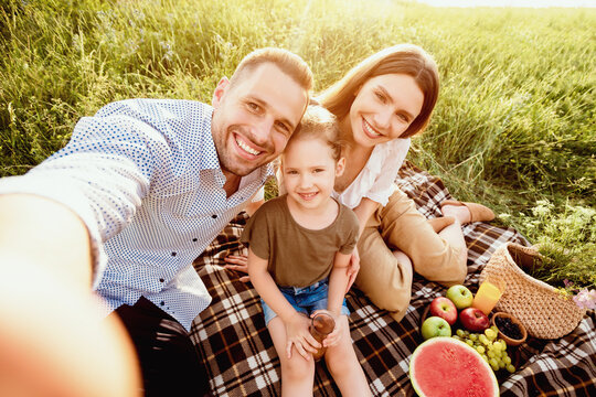 Vacation Concept. Top view of family taking selfie, sitting on the blanket in the countryside on a sunny day