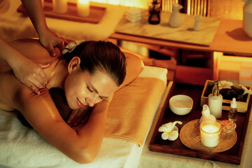 Caucasian woman customer enjoying relaxing anti-stress spa massage and pampering with beauty skin recreation leisure in warm candle lighting ambient salon spa at luxury resort or hotel. Quiescent