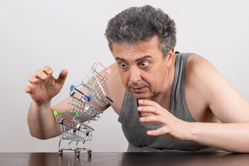 Conceptual story about poverty with a grey-haired middle-aged man and miniature empty shopping...