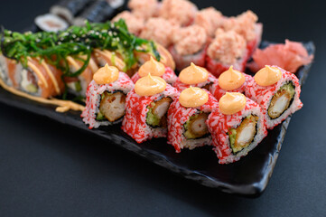Assorted sushi rolls with fish, shrimp, and seafood served on a black plate. Gourmet Japanese cuisine with colorful ingredients. Overhead view, minimal background.