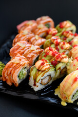 Assorted sushi rolls with fish, shrimp, and seafood served on a black plate. Gourmet Japanese cuisine with colorful ingredients. Overhead view, minimal background.
