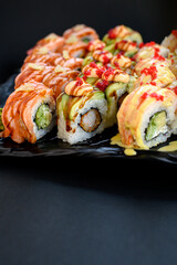 Assorted sushi rolls with fish, shrimp, and seafood served on a black plate. Gourmet Japanese cuisine with colorful ingredients. Overhead view, minimal background.