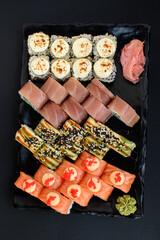 Assorted sushi rolls with fish, shrimp, and seafood served on a black plate. Gourmet Japanese cuisine with colorful ingredients. Overhead view, minimal background.