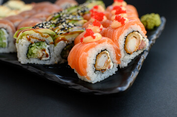 Assorted sushi rolls with fish, shrimp, and seafood served on a black plate. Gourmet Japanese cuisine with colorful ingredients. Overhead view, minimal background.