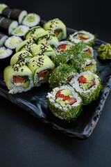 Assorted vegan sushi rolls served on a black plate. Colorful plant-based ingredients arranged in an elegant, minimalistic Japanese food presentation. Top view.