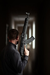 Naklejka premium man holding black tactical rifle in dim corridor interior